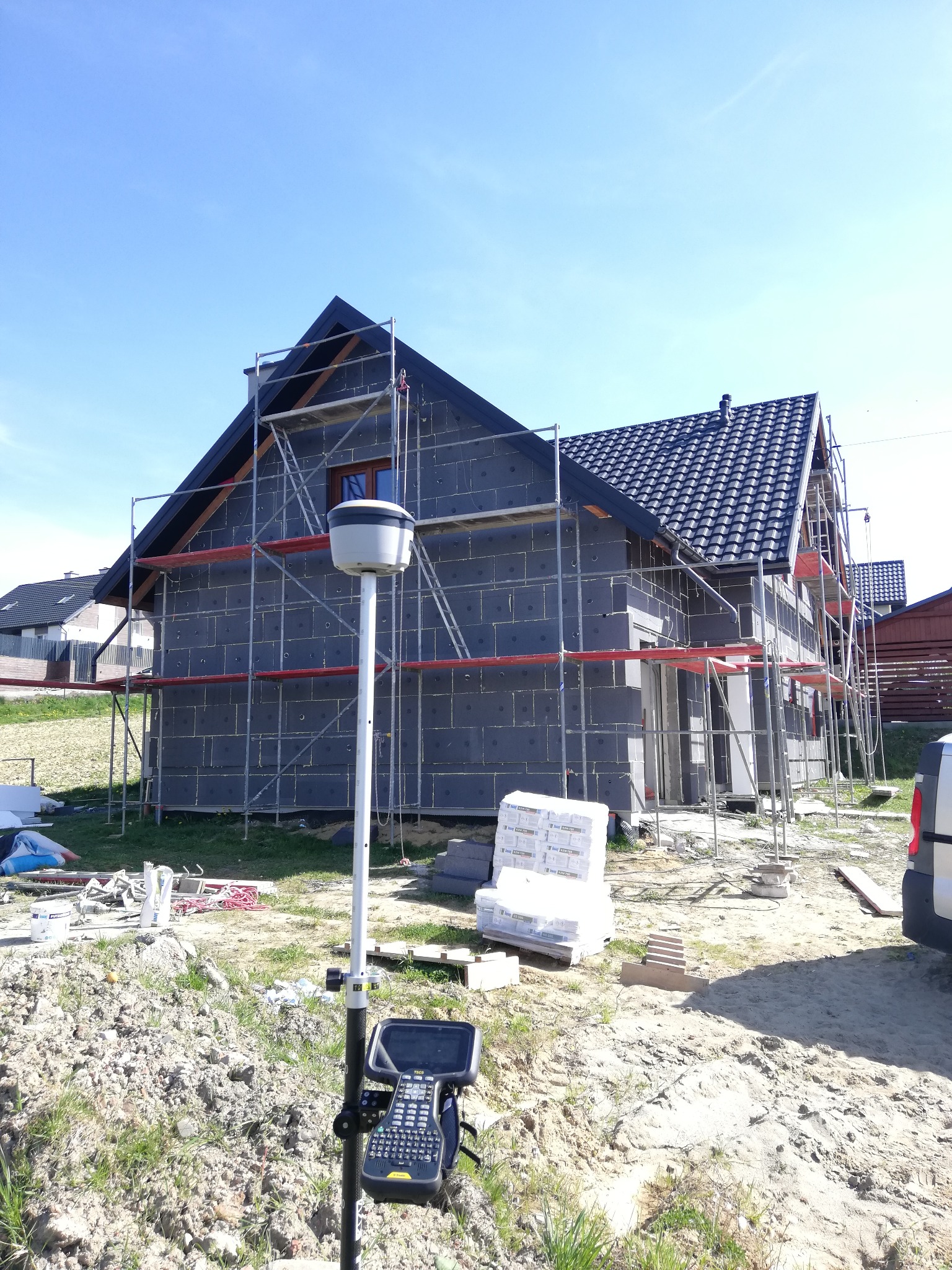 Dom w trakcie ocieplania, na rusztowaniach, z widocznym urządzeniem pomiarowym na pierwszym planie.