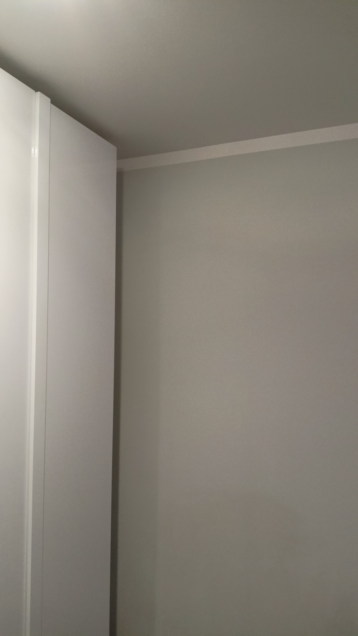 Pomieszczenie po remoncie: świeżo pomalowana ściana w odcieniach szarości, z widoczną białą listwą przypodłogową i narożnikiem szafy wnękowej.