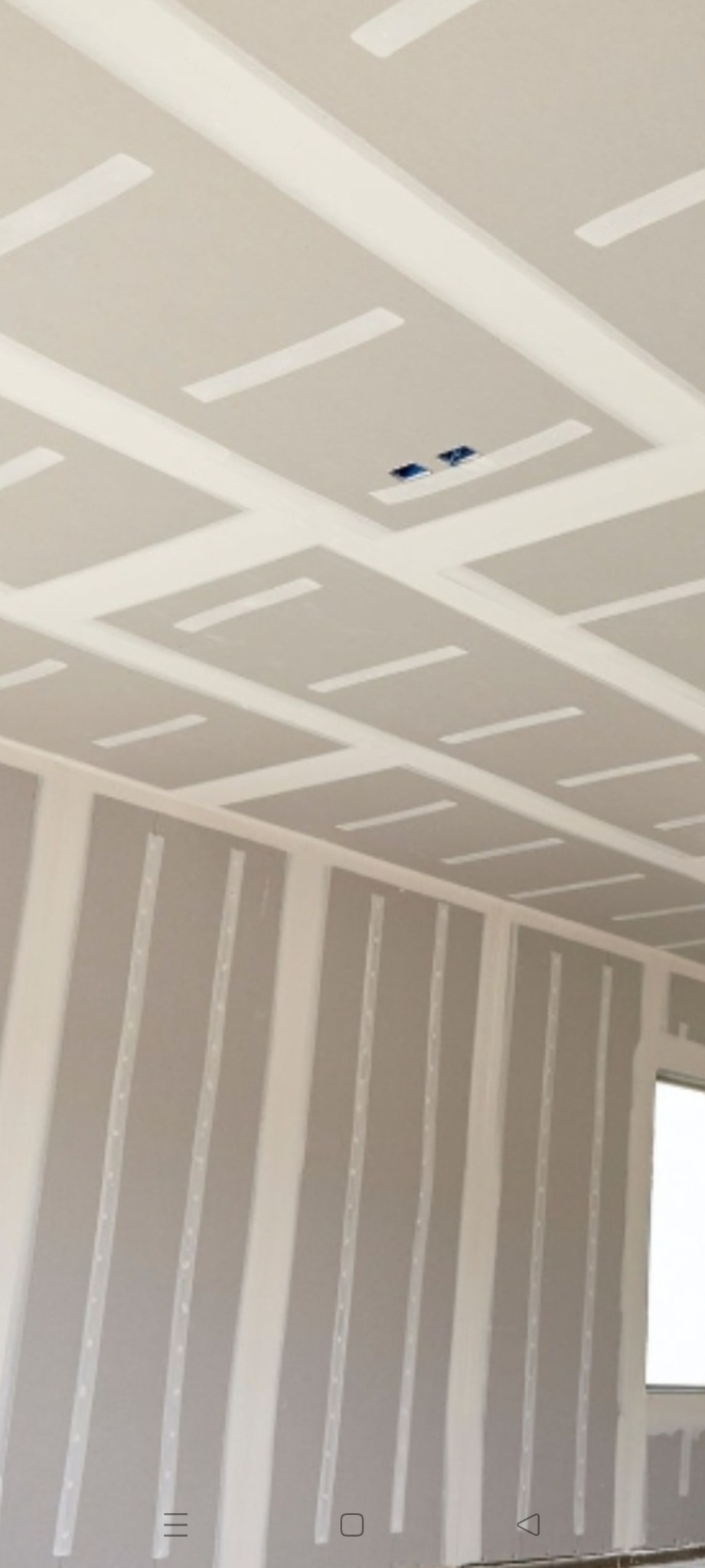 Ściana i sufit z płyt gipsowo-kartonowych, widoczne łączenia płyt wzmocnione taśmą, przygotowane do szpachlowania i malowania, z widocznymi otworami na gniazdka elektryczne w suficie.