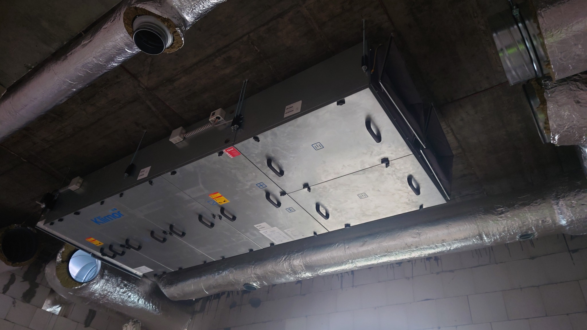 Centrala wentylacyjna Klimor zawieszona pod sufitem, widoczne rury wentylacyjne w izolacji aluminiowej.