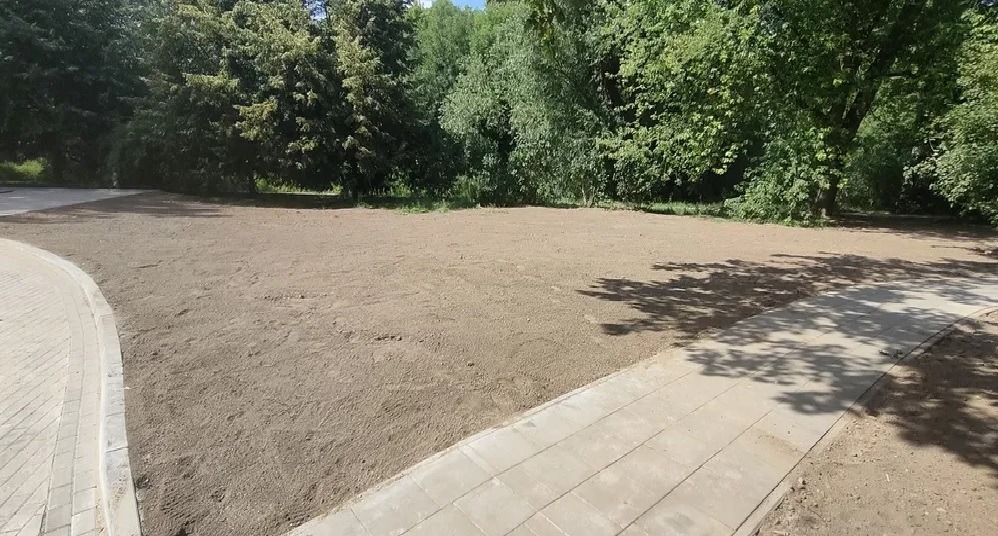 Wyrównany, przygotowany teren pod budowę z widocznym chodnikiem z kostki brukowej i otaczającą zielenią drzew.