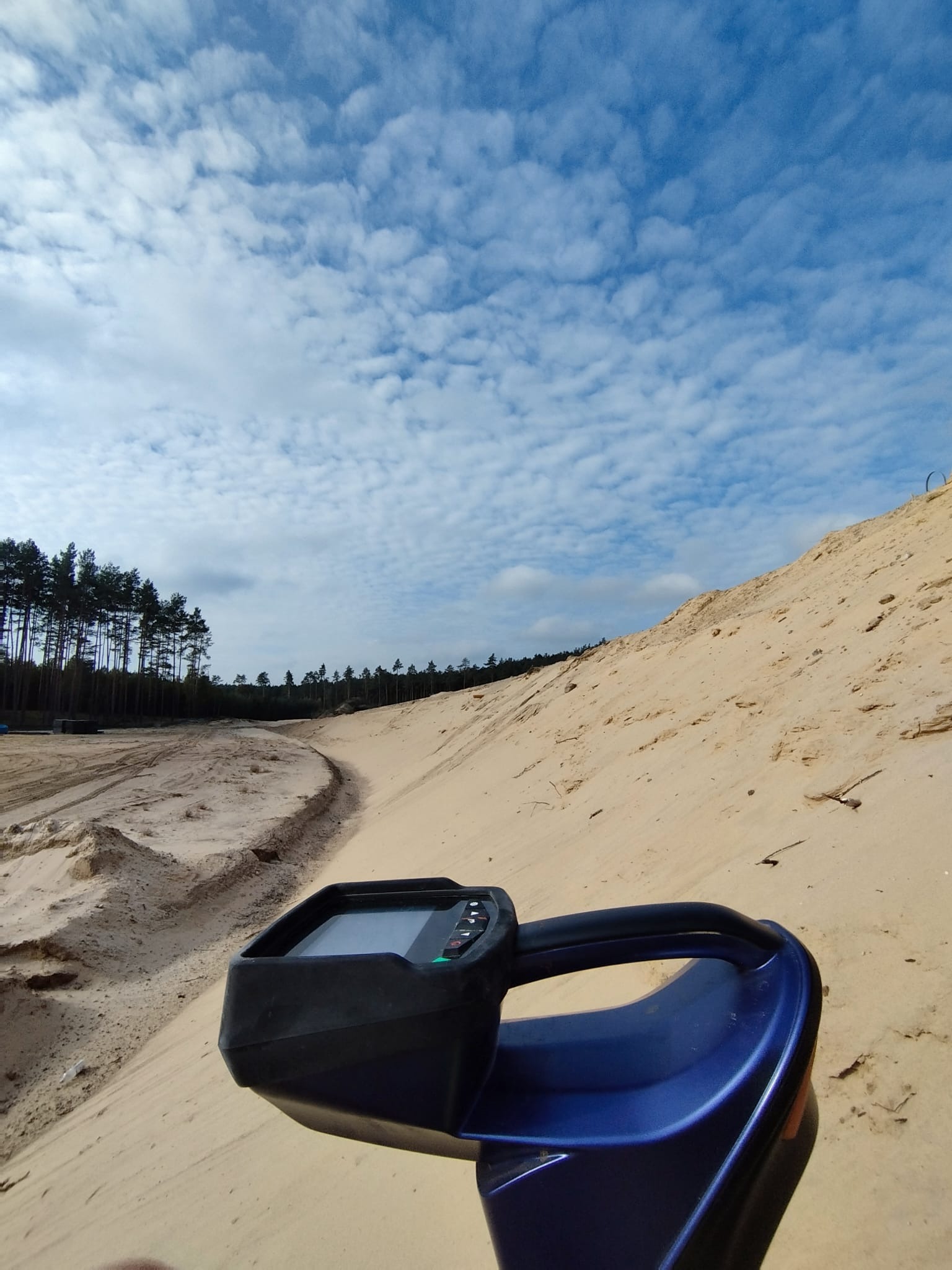 Niwelator laserowy na piaszczystym terenie budowy z widokiem na las i błękitne niebo. Sprzęt do niwelacji terenu w trakcie pracy.