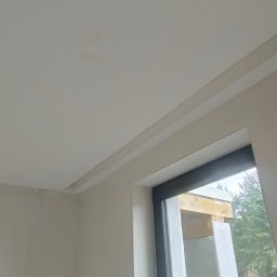 Karol Zep - Wykończone wnętrze z pomalowanymi ścianami w jasnym odcieniu i zamontowanym karniszem nad oknem, widoczne niedoskonałości na suficie.