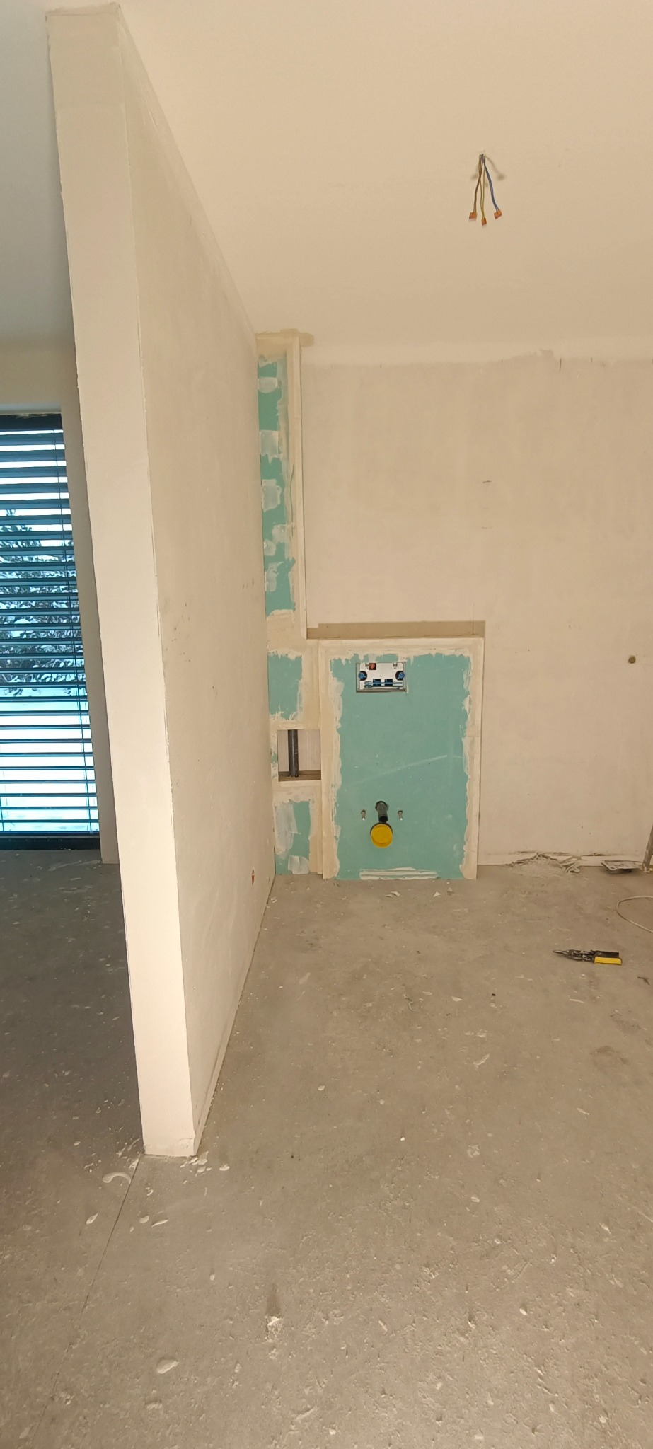 Wnętrze łazienki w trakcie przygotowania pod zabudowę stelaża WC z widocznymi płytami kartonowo-gipsowymi, instalacją hydrauliczną i przygotowanymi przewodami elektrycznymi.