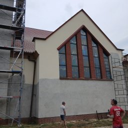 Nazar hulenchin - Kościół w trakcie prac elewacyjnych, widoczne rusztowania i fragmenty nieotynkowanej ściany, okna witrażowe z ceglaną obramówką.
