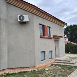 Nazar hulenchin - Ściana budynku po nałożeniu szarego tynku w Piasecznie, widoczny klimatyzator na elewacji i ceglana podmurówka.