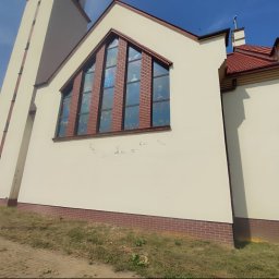 Nazar hulenchin - Kościół z beżową elewacją, czerwonym dachem i witrażowymi oknami, na ścianie widoczne ślady po usuniętych napisach, na pierwszym planie trawa i chodnik, w tle błękitne niebo.