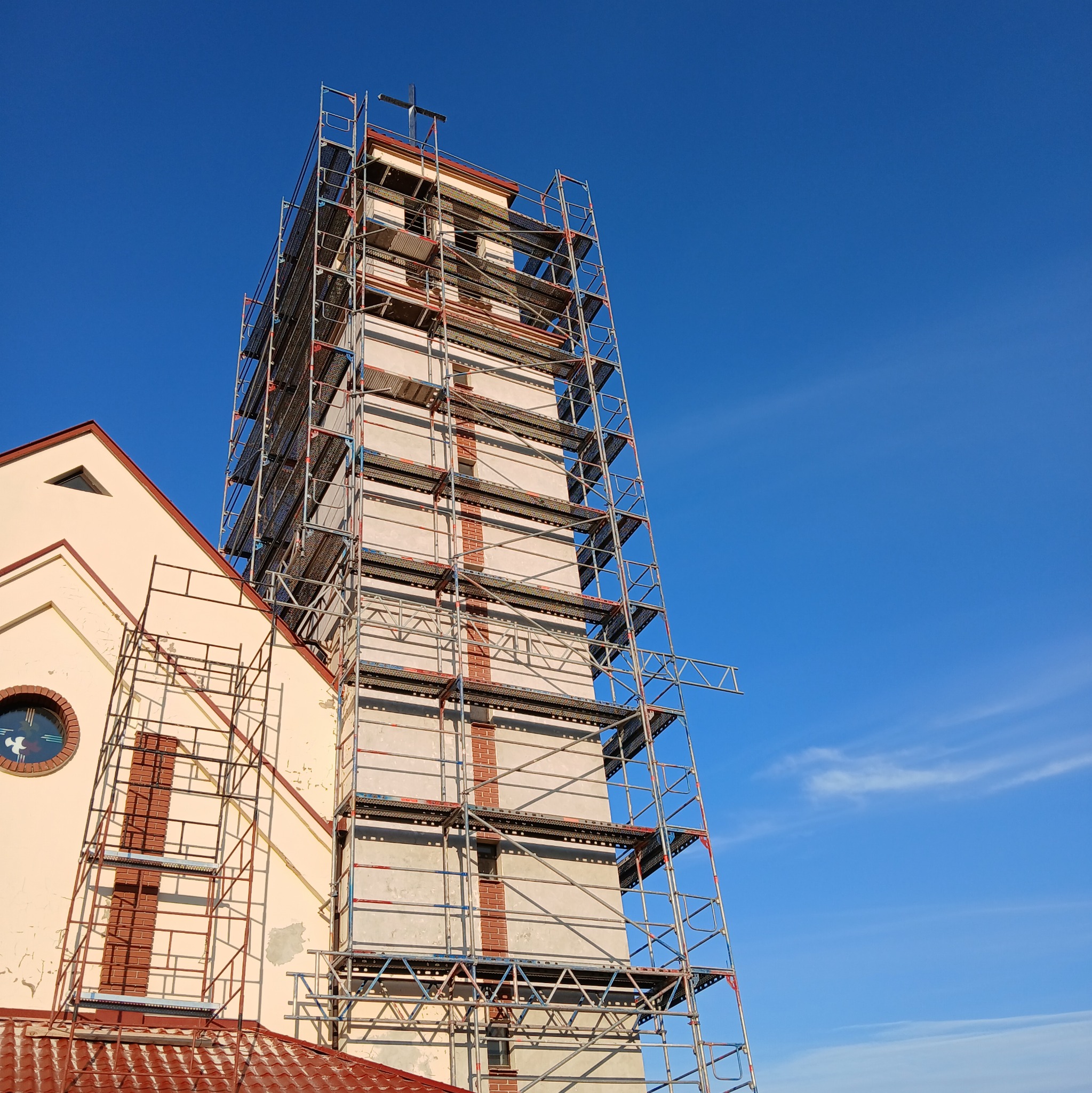 Wieża kościoła w rusztowaniach podczas prac renowacyjnych, błękitne niebo w tle.