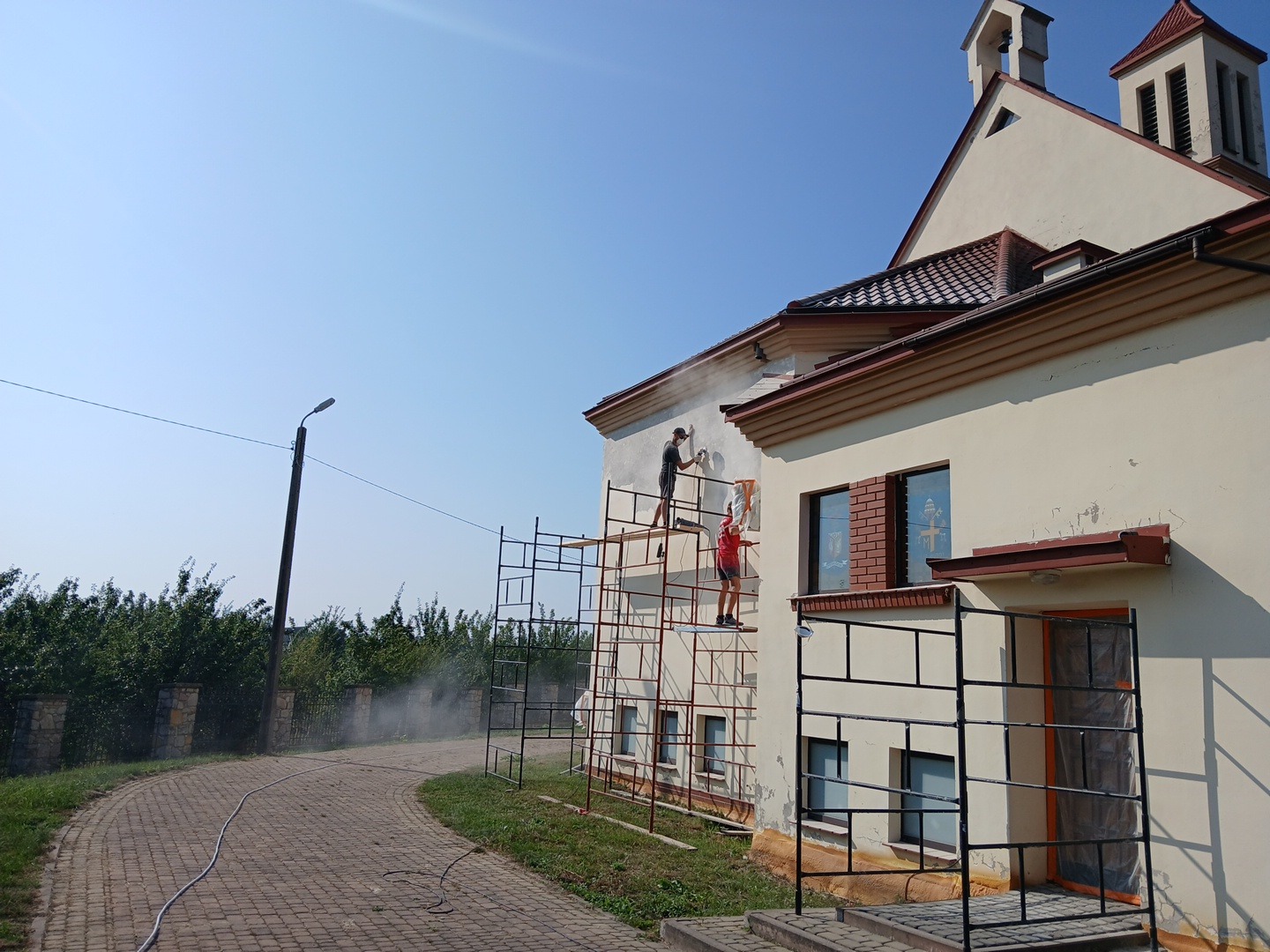 Dwóch pracowników na rusztowaniu czyści elewację budynku sakralnego pod wysokim ciśnieniem, przygotowując ją do dalszych prac.