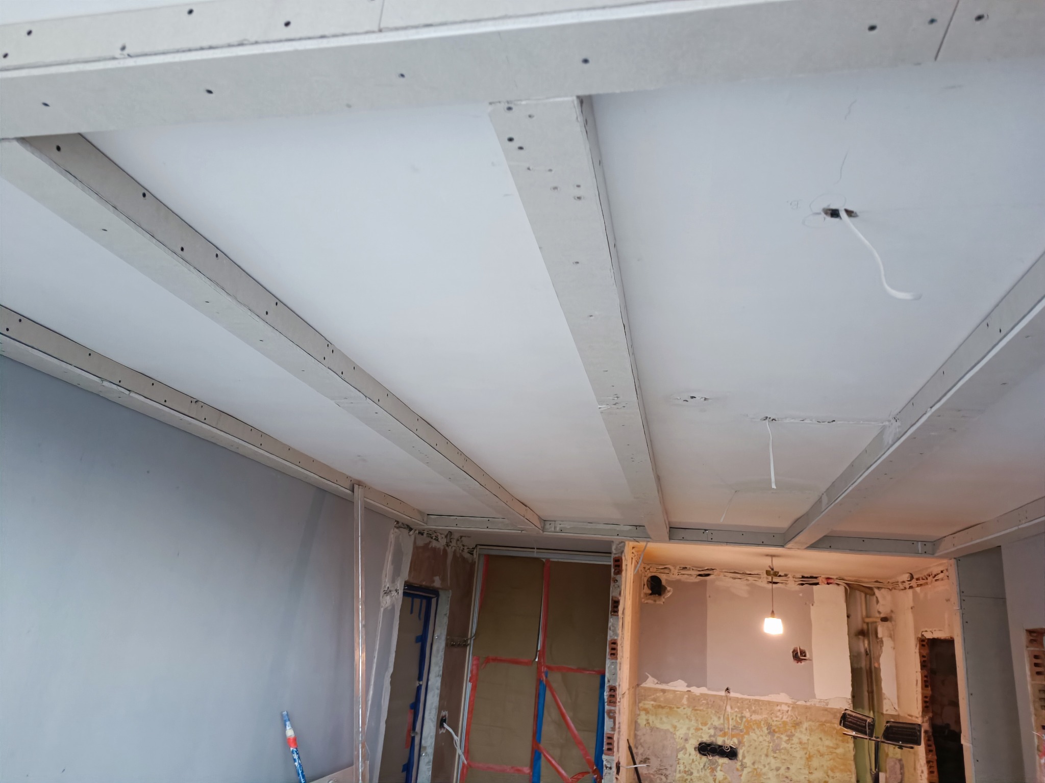 Montaż sufitu podwieszanego z płyty karton gips, widoczne profile i płyty, instalacja elektryczna w trakcie prac, surowe ściany w tle.