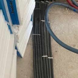 LDM Marta Teslar - Rury instalacyjne w peszlach, przymocowane do ściany na etapie montażu, obok stos styropianu.