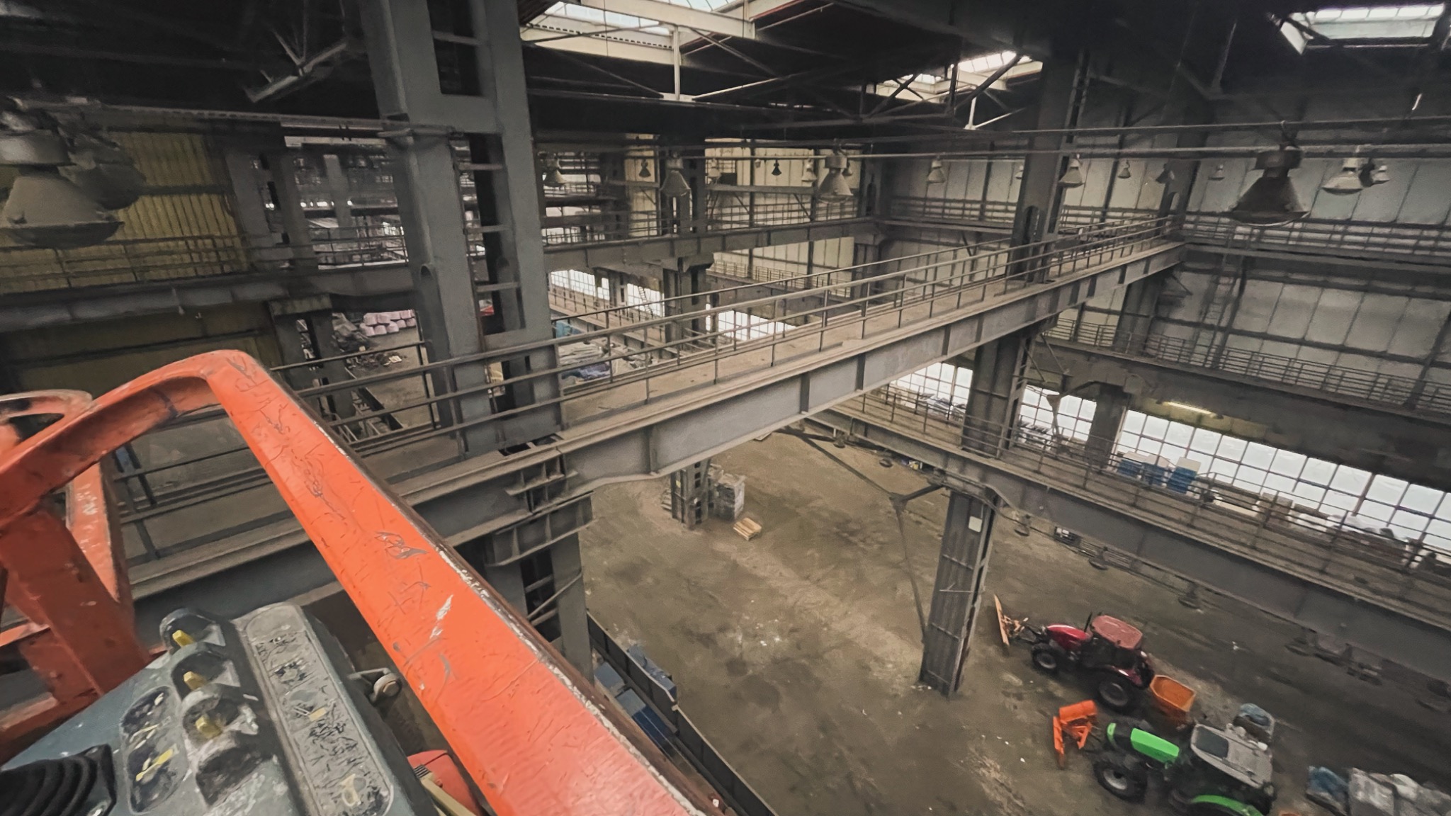 Wysoka hala przemysłowa z metalowymi konstrukcjami, widok z podnośnika koszowego na zainstalowane oświetlenie i pomosty komunikacyjne.