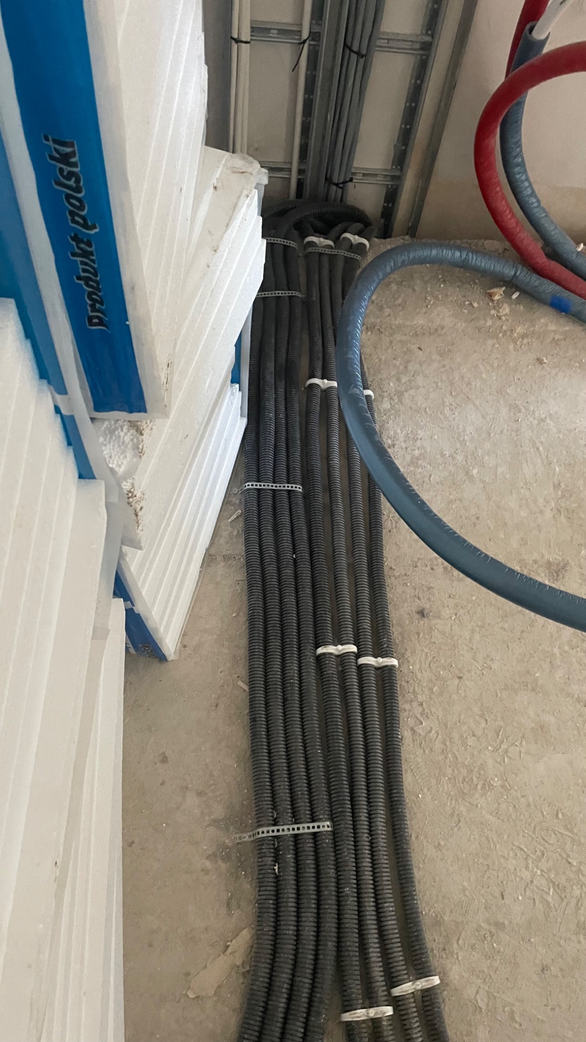 Rury instalacyjne w peszlach, przymocowane do ściany na etapie montażu, obok stos styropianu.