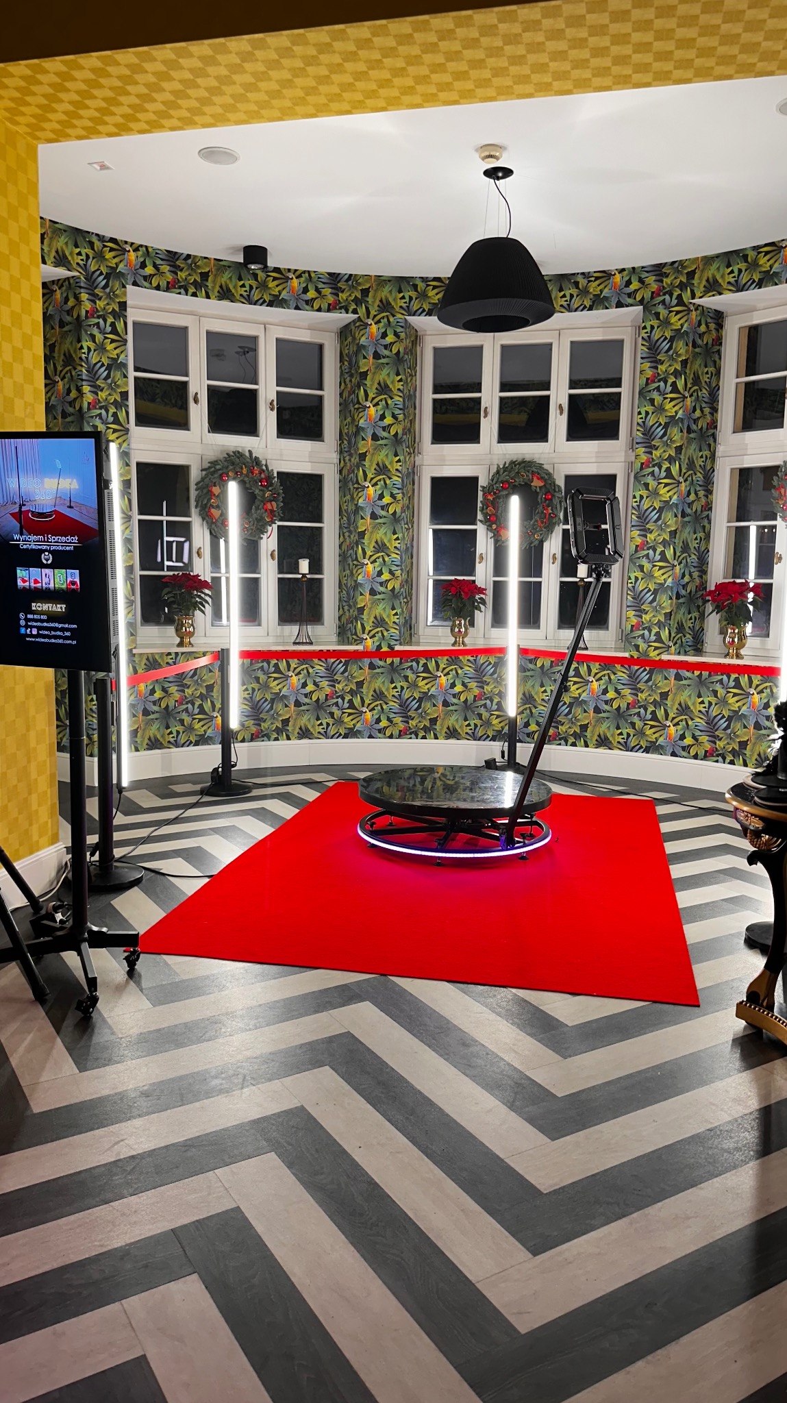 Wnętrze z przygotowaną platformą obrotową 360 stopni na czerwonym dywanie, otoczoną lampami LED, ekranem reklamowym i dekoracjami świątecznymi.