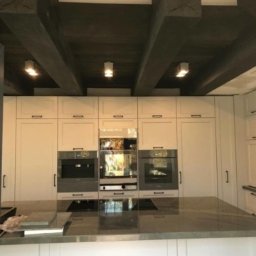 OMEGA TOMASZ KRĘCIOCH - Nowoczesna kuchnia z białymi szafkami, szarym blatem i drewnianymi belkami sufitowymi z oświetleniem punktowym. Minimalistyczny design.