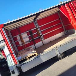 Nona trans - Otwarta przestrzeń ładunkowa busa z czerwonymi zasłonami, częściowo załadowana paleta z towarem, widok z boku na kabinę kierowcy.