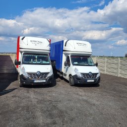 Nona trans - Dwa białe busy Renault Master z nadbudówkami, zaparkowane obok siebie na żwirowym placu, z widocznym logo firmy 'NONA Trans' i numerami telefonów na nadbudówkach, przed betonowym ogrodzeniem...