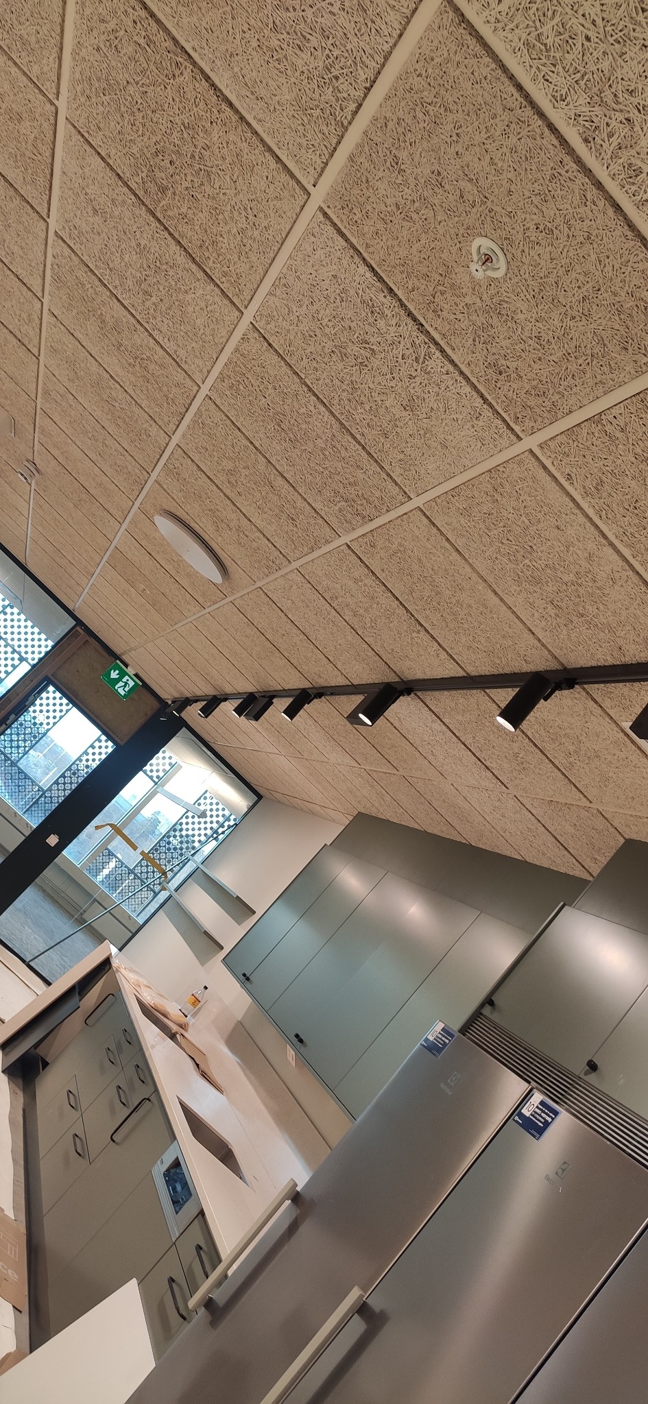 Biuro po remoncie: widok na sufit z paneli akustycznych, oświetlenie punktowe, okno z żaluzjami i zabudowę meblową ze sprzętem AGD