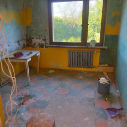 Roman Korolchuk - Kadr z remontowanej łazienki: ściany z resztkami farby, okno z widokiem na zieleń, grzejnik, narzędzia. Stan 'przed' z widocznym bałaganem.