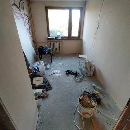 Roman Korolchuk - Pokój w trakcie remontu: surowe ściany, okno, narzędzia i materiały budowlane. Widoczne ślady po wcześniejszych pracach. Stan 'przed' wykończeniem wnętrza.