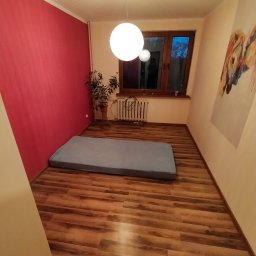 Roman Korolchuk - Pokój po malowaniu ścian na różowo i ułożeniu paneli podłogowych w odcieniach brązu. Na podłodze leży materac. Na ścianie wisi obraz. Widok z góry.