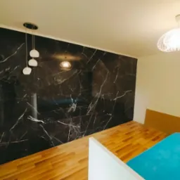 Wykończony pokój z panelami podłogowymi i ścianą z płytek imitujących czarny marmur. Widoczne lampy sufitowe.