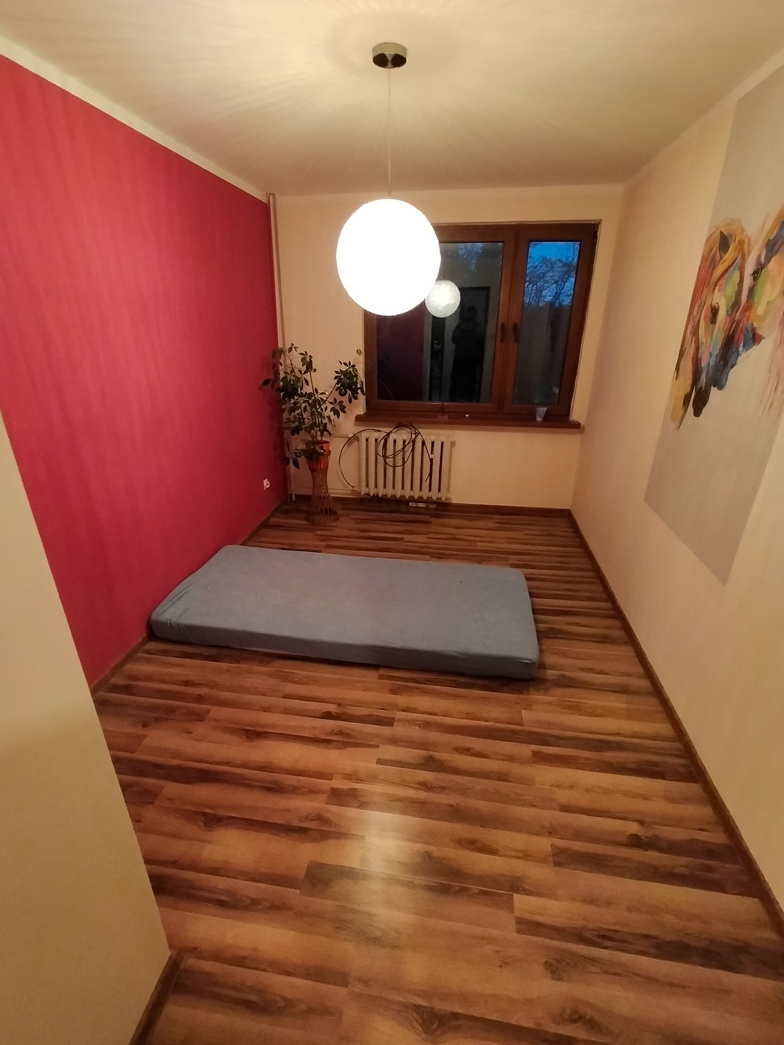 Pokój po malowaniu ścian na różowo i ułożeniu paneli podłogowych w odcieniach brązu. Na podłodze leży materac. Na ścianie wisi obraz. Widok z góry.