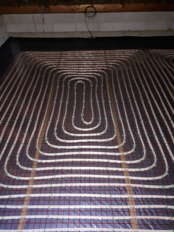 Rozłożona instalacja ogrzewania podłogowego z rurkami przymocowanymi do siatki, widok z góry na surową podłogę przed wylaniem wylewki.