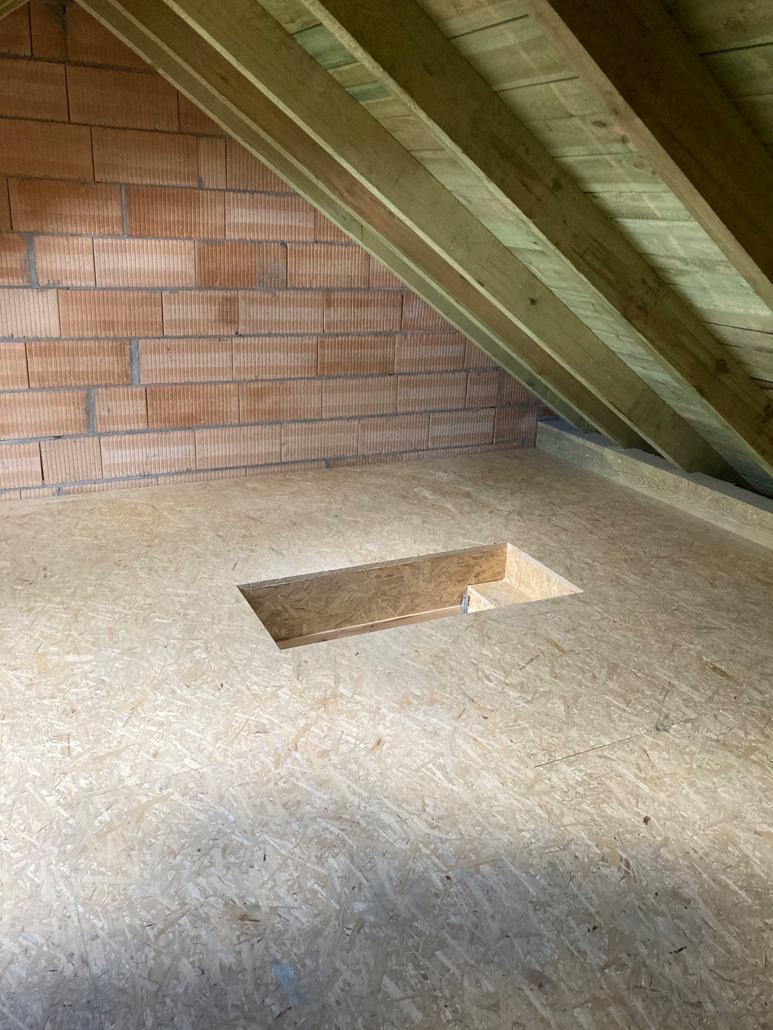 Podłoga z płyt OSB na poddaszu z otworem rewizyjnym, widoczne krokwie i fragment ściany z cegły dziurawki