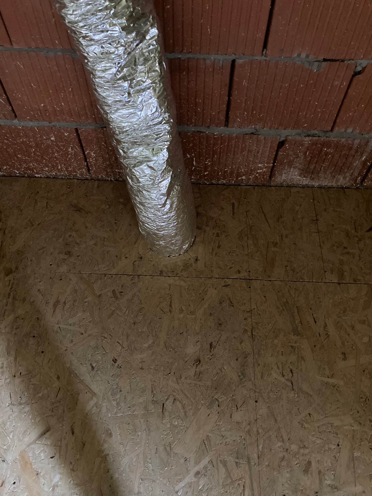 Izolowany przewód wentylacyjny z folii aluminiowej zamontowany na surowym suficie z cegły i płycie OSB poddasza.