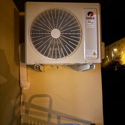 Kacper Goraj Instalacje i Serwis INSTALLERS - Zewnętrzna jednostka klimatyzacji GREE zamontowana na balkonie budynku mieszkalnego, widoczna instalacja odprowadzająca skropliny, nocne oświetlenie.