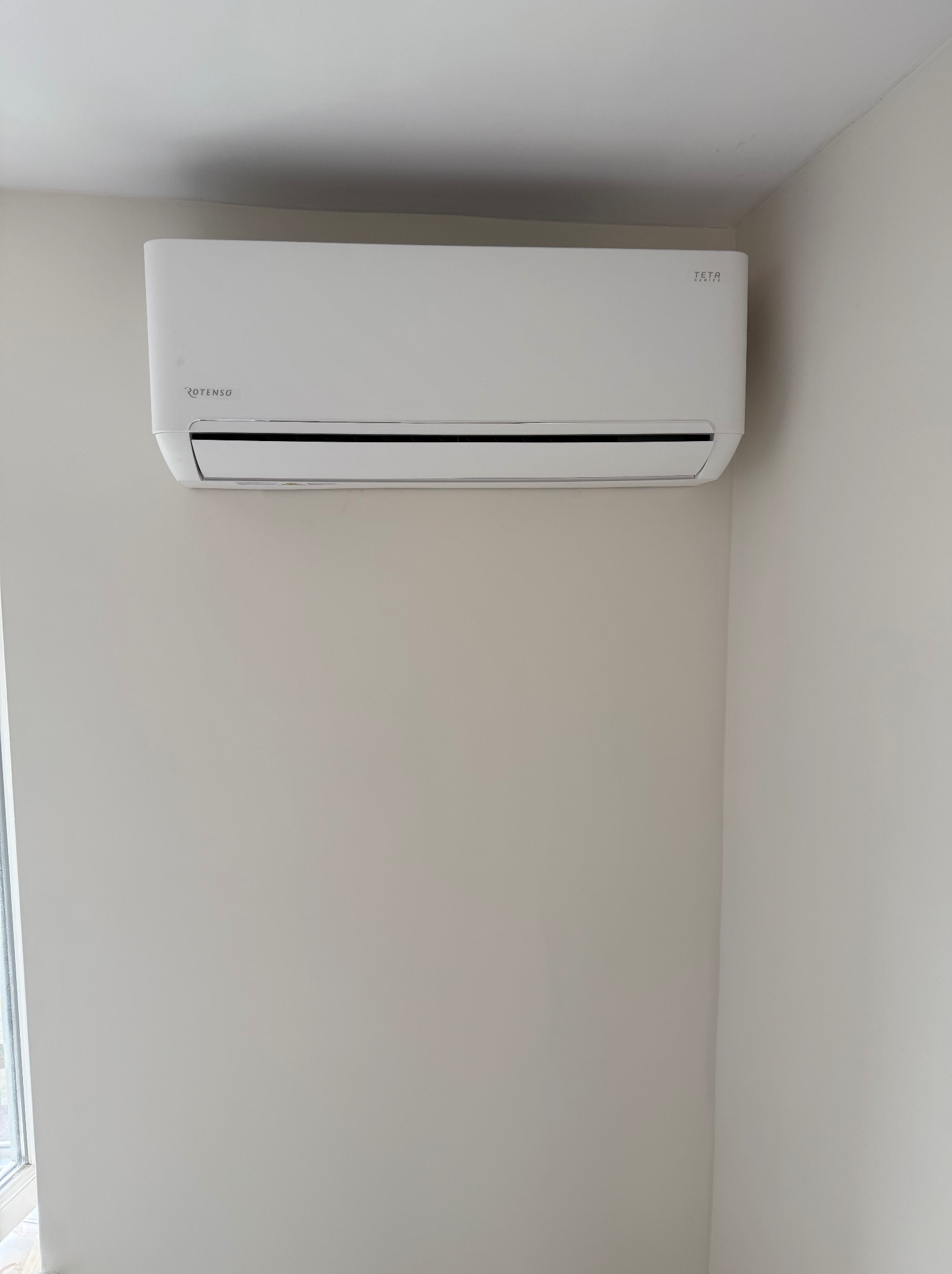Biała klimatyzacja Rotenso Teta Series zamontowana na jasnej ścianie w rogu pokoju.