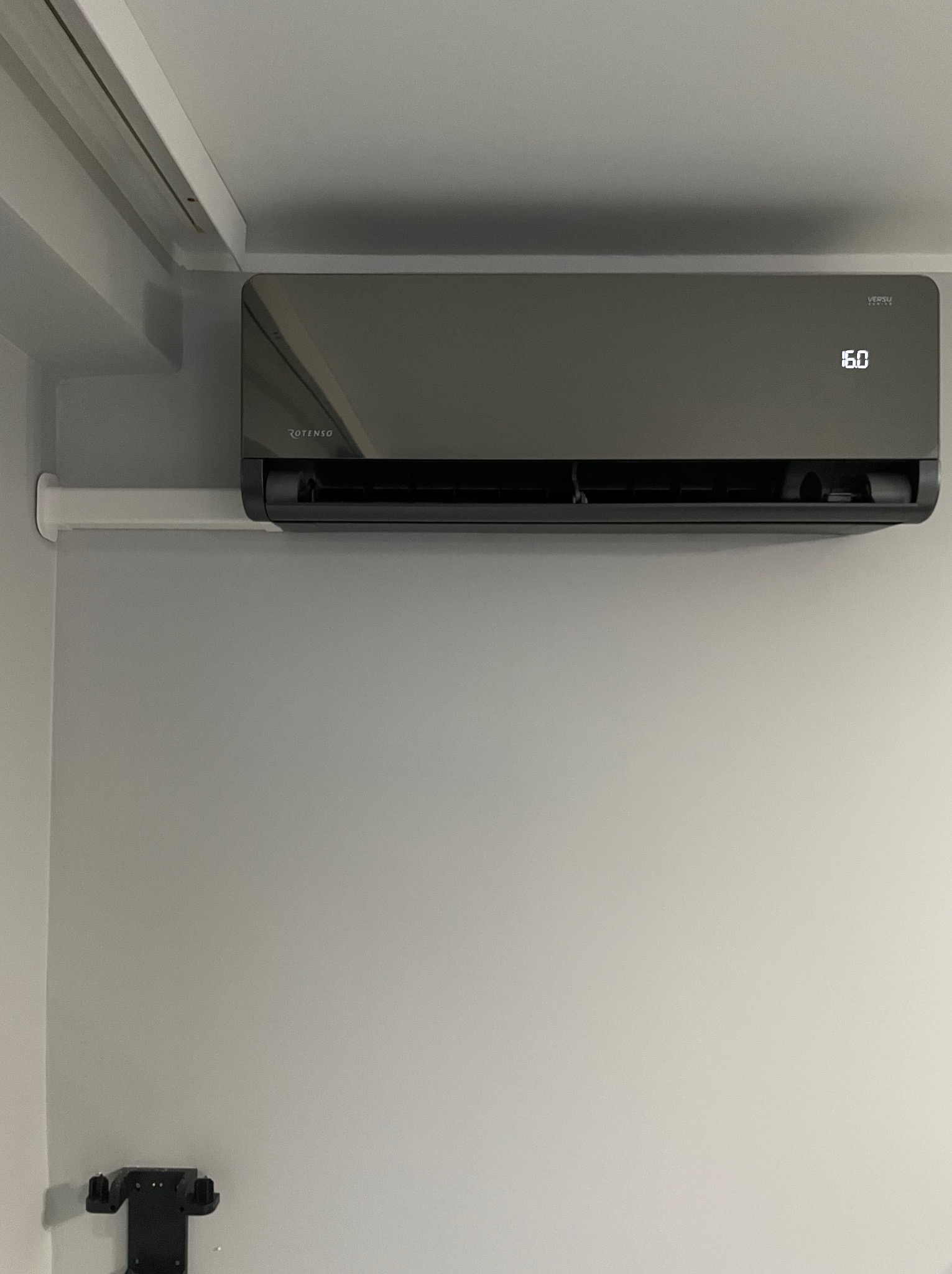 Czarny klimatyzator Rotenso Versu zamontowany na ścianie, wyświetlający temperaturę 16 stopni Celsjusza, z widoczną instalacją elektryczną poniżej.
