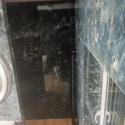 Pro-Efekt Przemysław Zimoch - Luksusowa łazienka z marmurowymi ścianami w odcieniach szarości i zieleni, kabina prysznicowa ze szklanymi drzwiami, drewniana podłoga i okrągłe lustro.