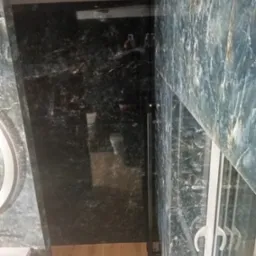 Luksusowa łazienka z marmurowymi ścianami w odcieniach szarości i zieleni, kabina prysznicowa ze szklanymi drzwiami, drewniana podłoga i okrągłe lustro.