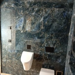 Pro-Efekt Przemysław Zimoch - Elegancka łazienka z marmurowymi płytkami w odcieniach granatu i brązu. Wiszący bidet i toaleta, drewniana podłoga, minimalistyczne oświetlenie sufitowe.