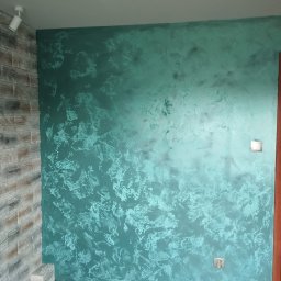 Pro-Efekt Przemysław Zimoch - Ściana z dekoracyjną, turkusową farbą strukturalną, imitującą efekt aksamitu, z fragmentem ściany wykończonej kamieniem dekoracyjnym po lewej stronie.