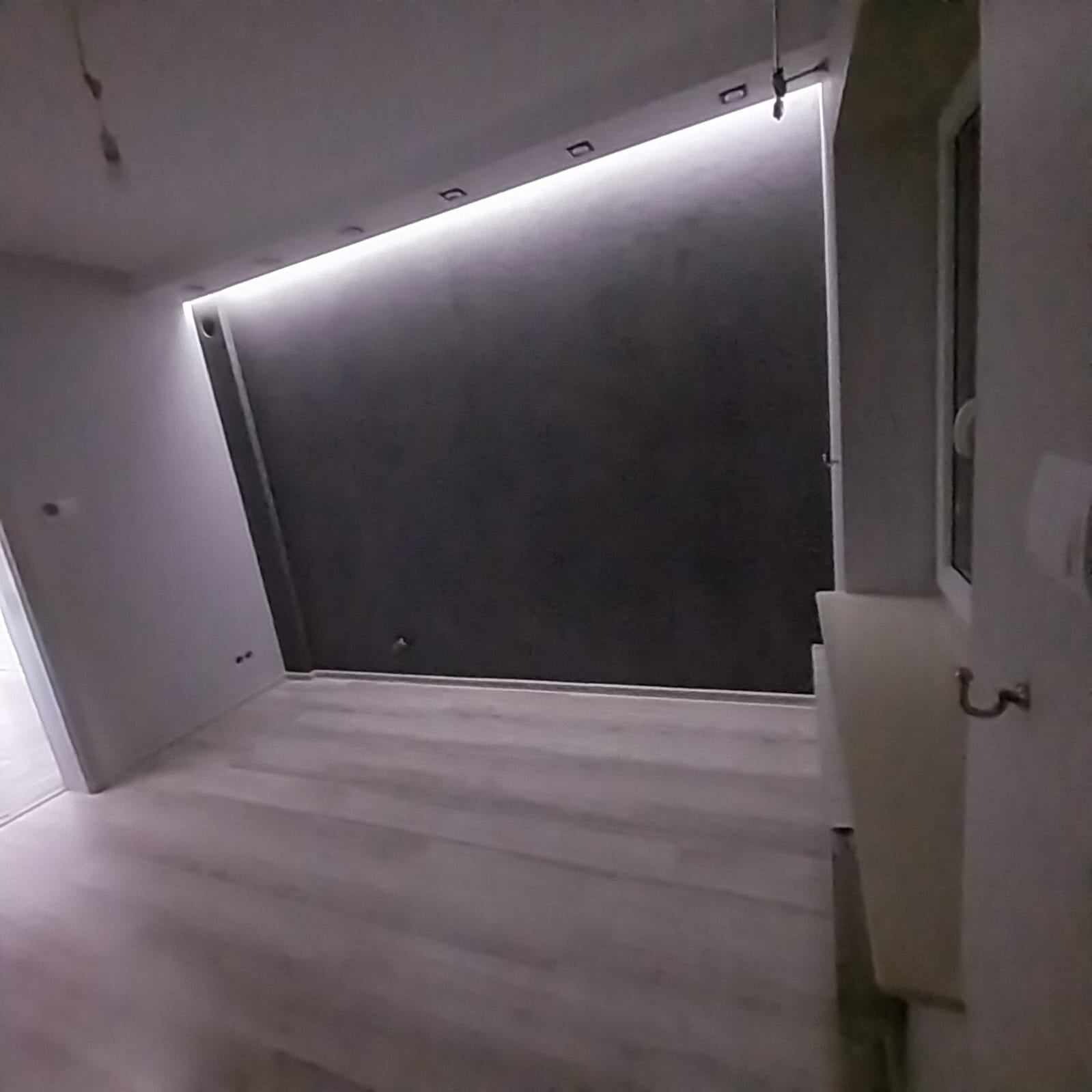 Nowoczesne wnętrze po remoncie z ciemną ścianą podświetloną ledami, jasną podłogą i fragmentem okna.