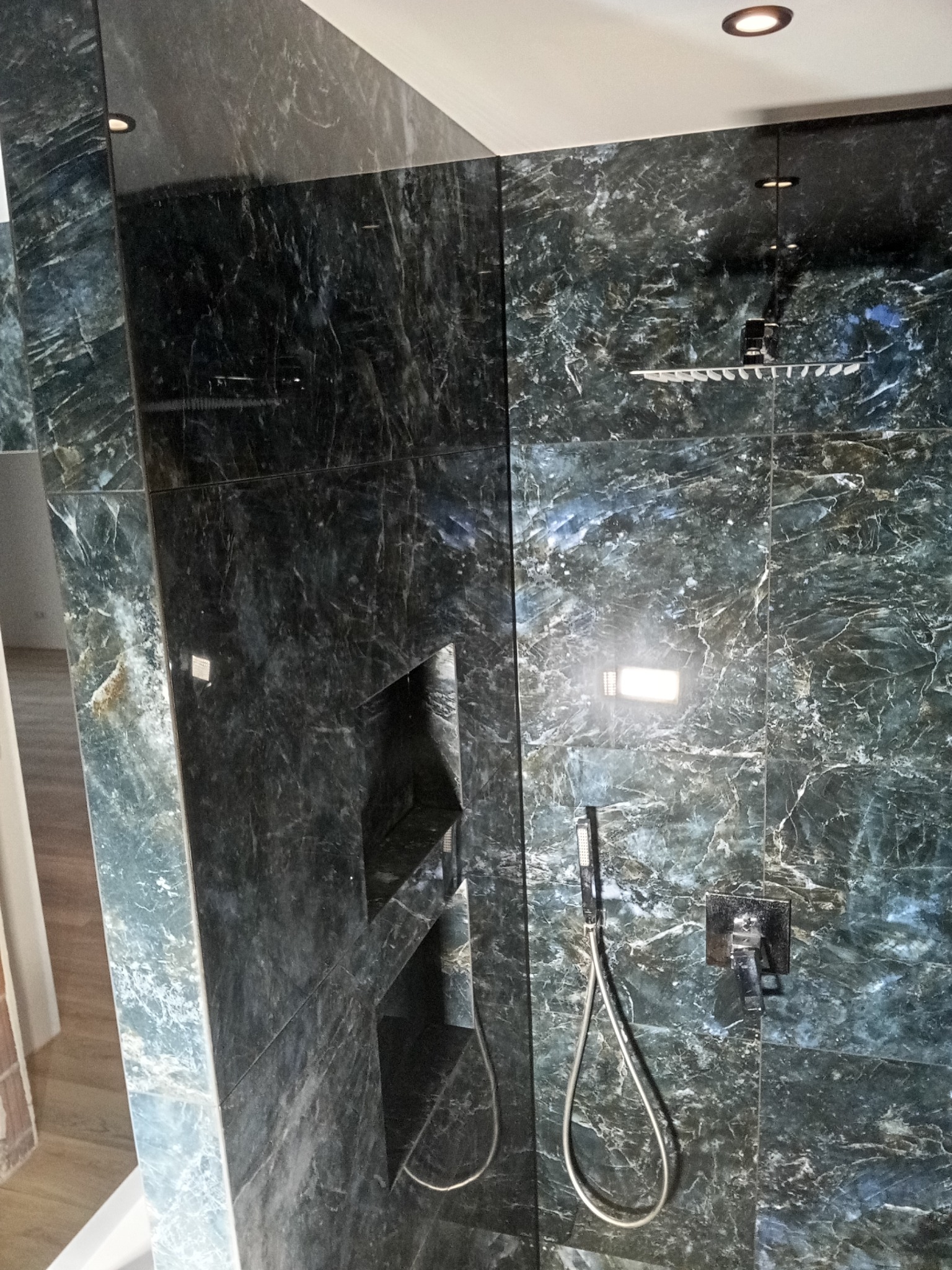 Luksusowy prysznic typu walk-in z ciemnozielonymi, marmurkowymi płytkami, wbudowanymi półkami i deszczownicą. Nowoczesny design z eleganckimi detalami.