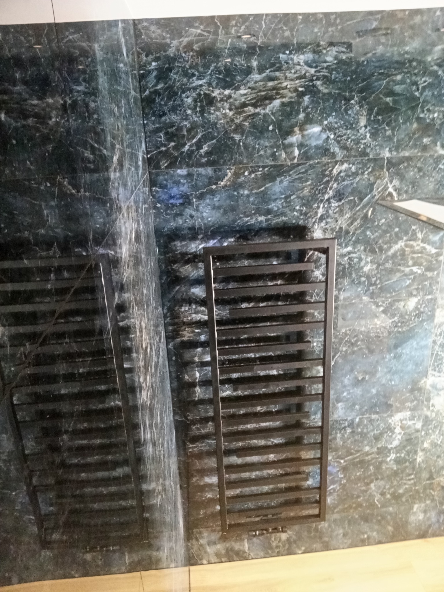 Łazienka z płytkami imitującymi marmur i czarnym grzejnikiem drabinkowym. Wykończenie z dbałością o detale, nowoczesny design.