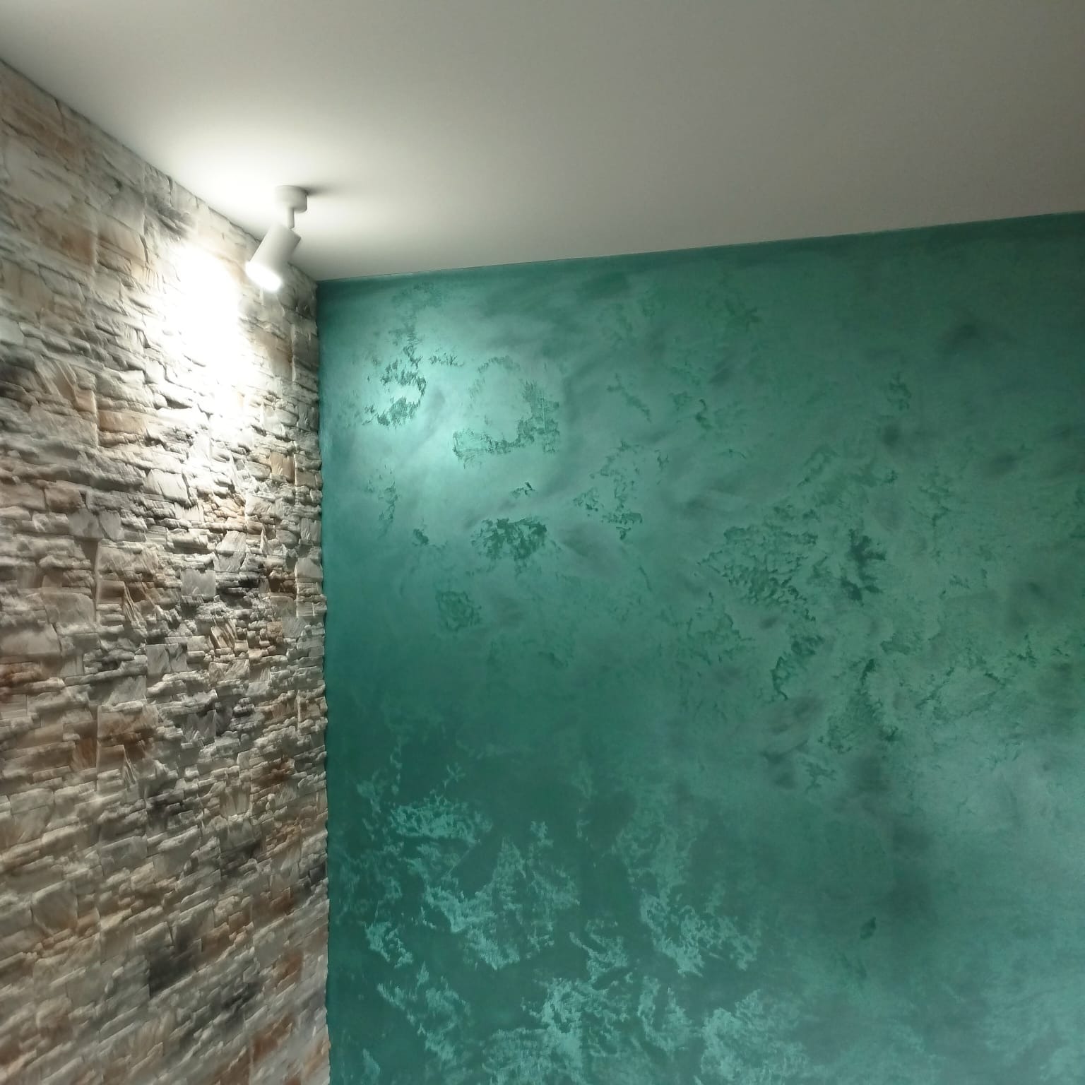 Wykończenie ściany: dekoracyjna, turkusowa farba strukturalna i panel imitujący kamień, oświetlone punktowo. Nowoczesny design wnętrza.