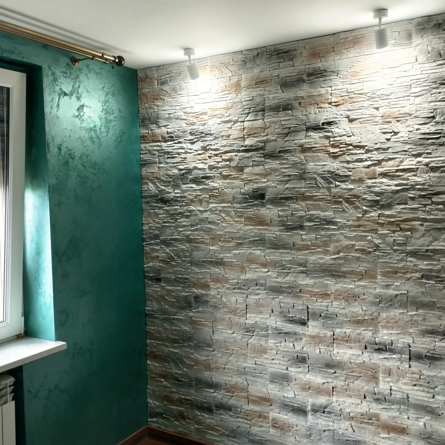 Wykończenie wnętrza: ściana z dekoracyjną strukturą kamienia i zielona ściana z efektem ombre, oświetlona punktowymi lampami sufitowymi, widok na okno.