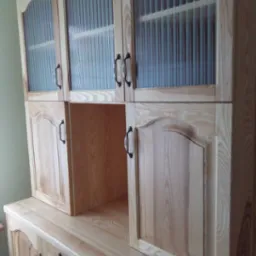 Drewniana zabudowa kuchenna z ryflowanymi szklanymi frontami szafek wiszących, widoczne metalowe uchwyty i naturalny odcień drewna.