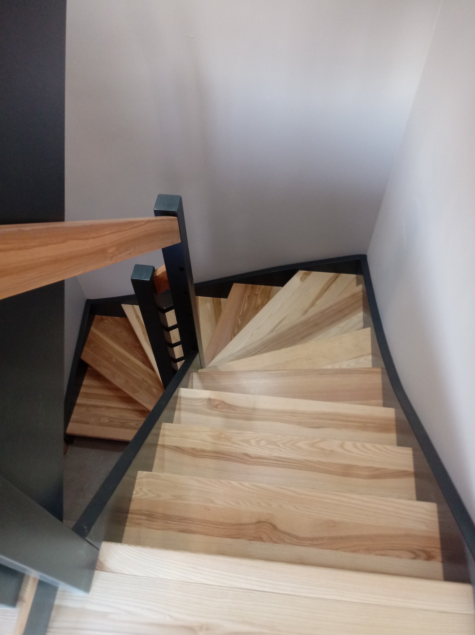 Spiralne schody drewniane z jasnego drewna z czarnymi elementami konstrukcyjnymi, widok z góry.