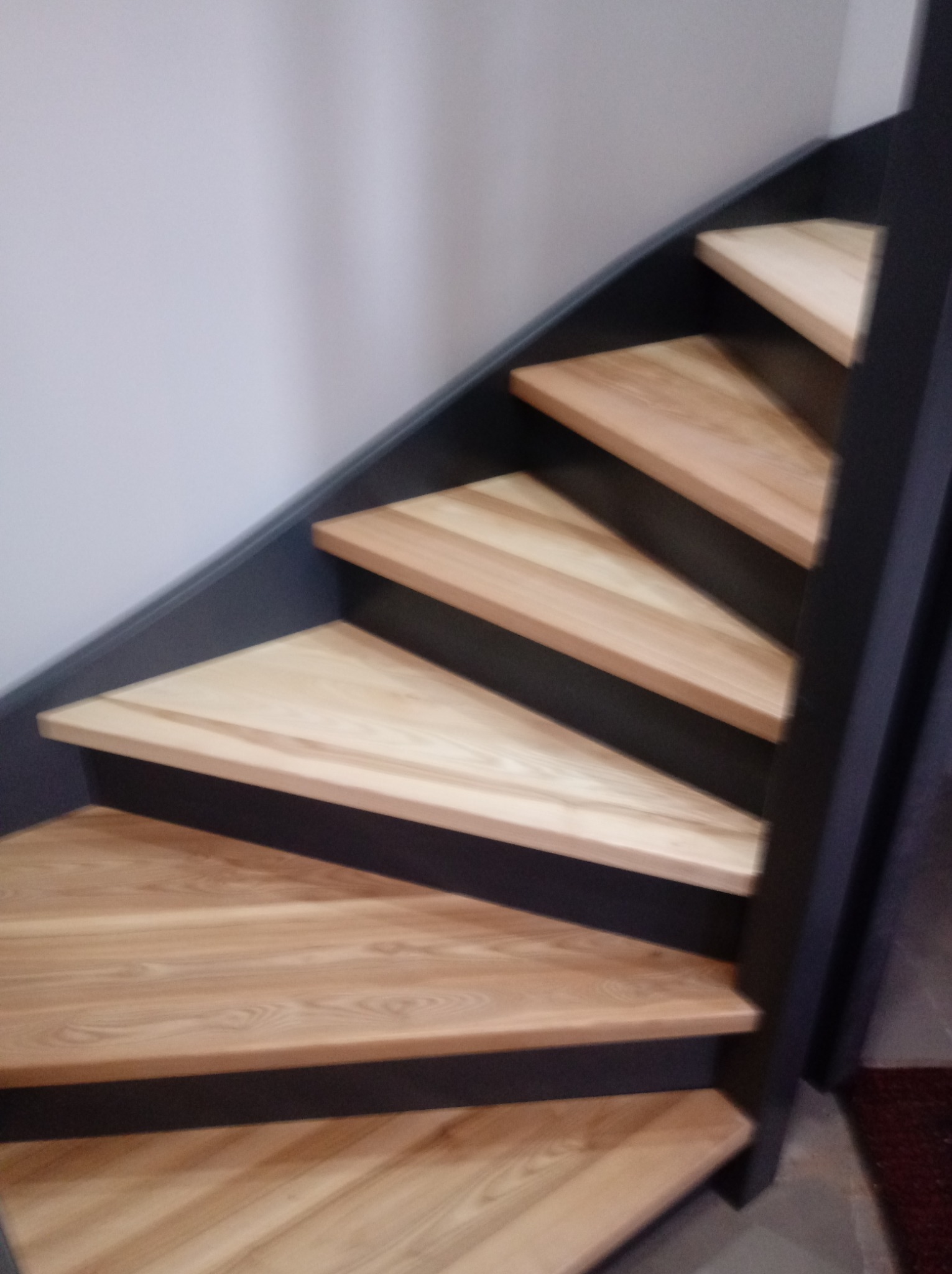 Kątowe schody z jasnego drewna z ciemnymi podstopnicami i barierką, widok z dołu.