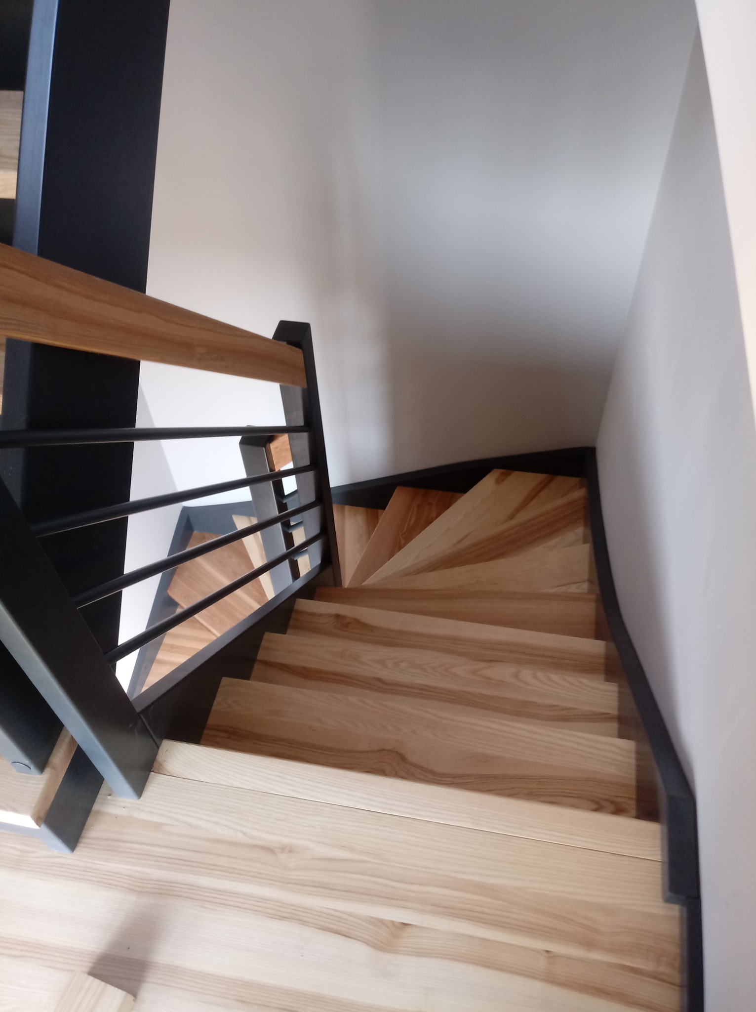 Widok z góry na jasne, drewniane schody z czarnymi balustradami i metalowymi wypełnieniami w domu w Głogowie.