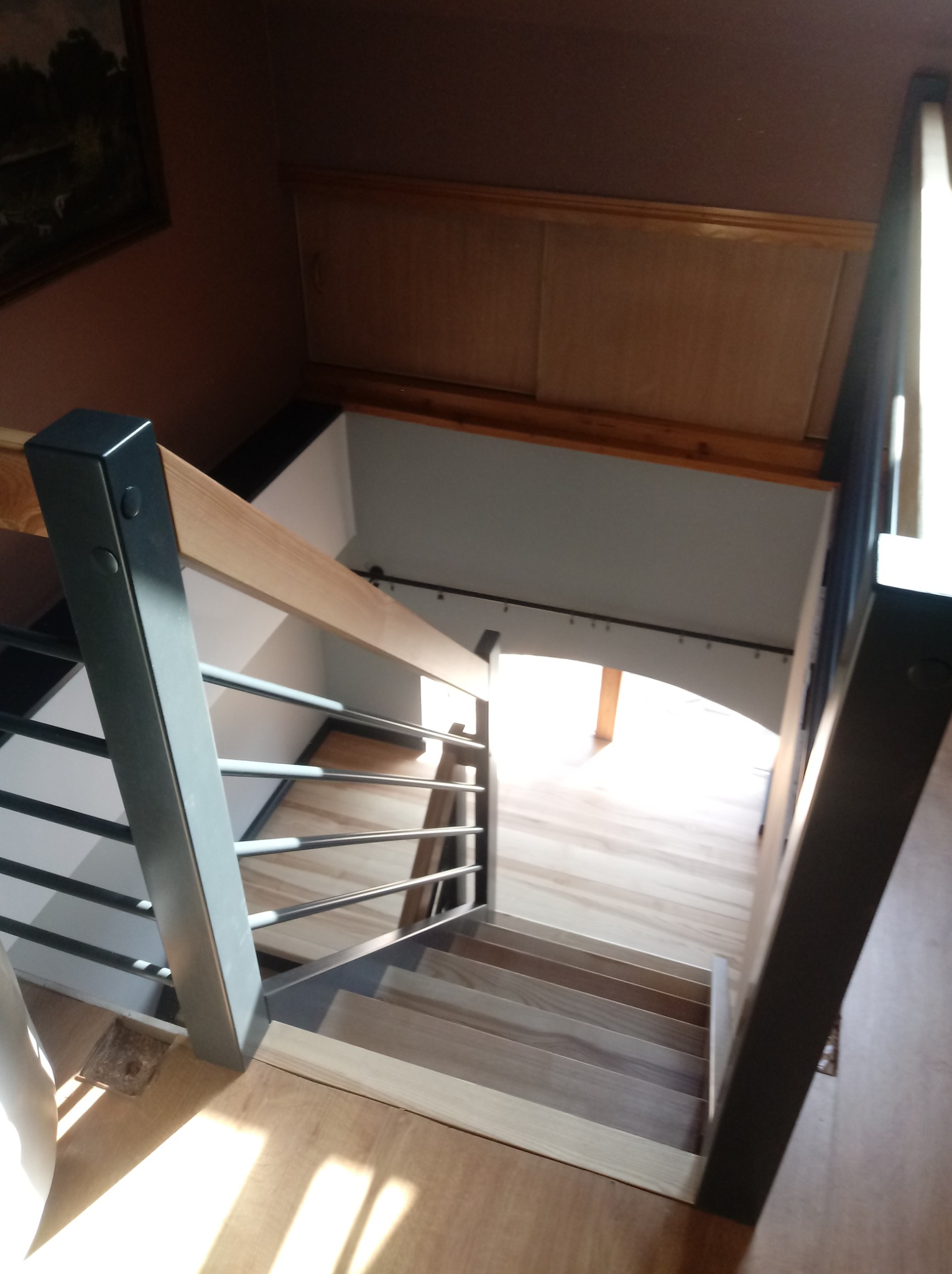 Wewnętrzne schody z jasnego drewna z metalowymi balustradami, widok z góry na dół, naturalne oświetlenie.