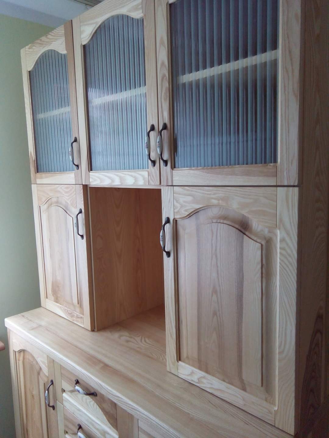 Drewniana zabudowa kuchenna z ryflowanymi szklanymi frontami szafek wiszących, widoczne metalowe uchwyty i naturalny odcień drewna.