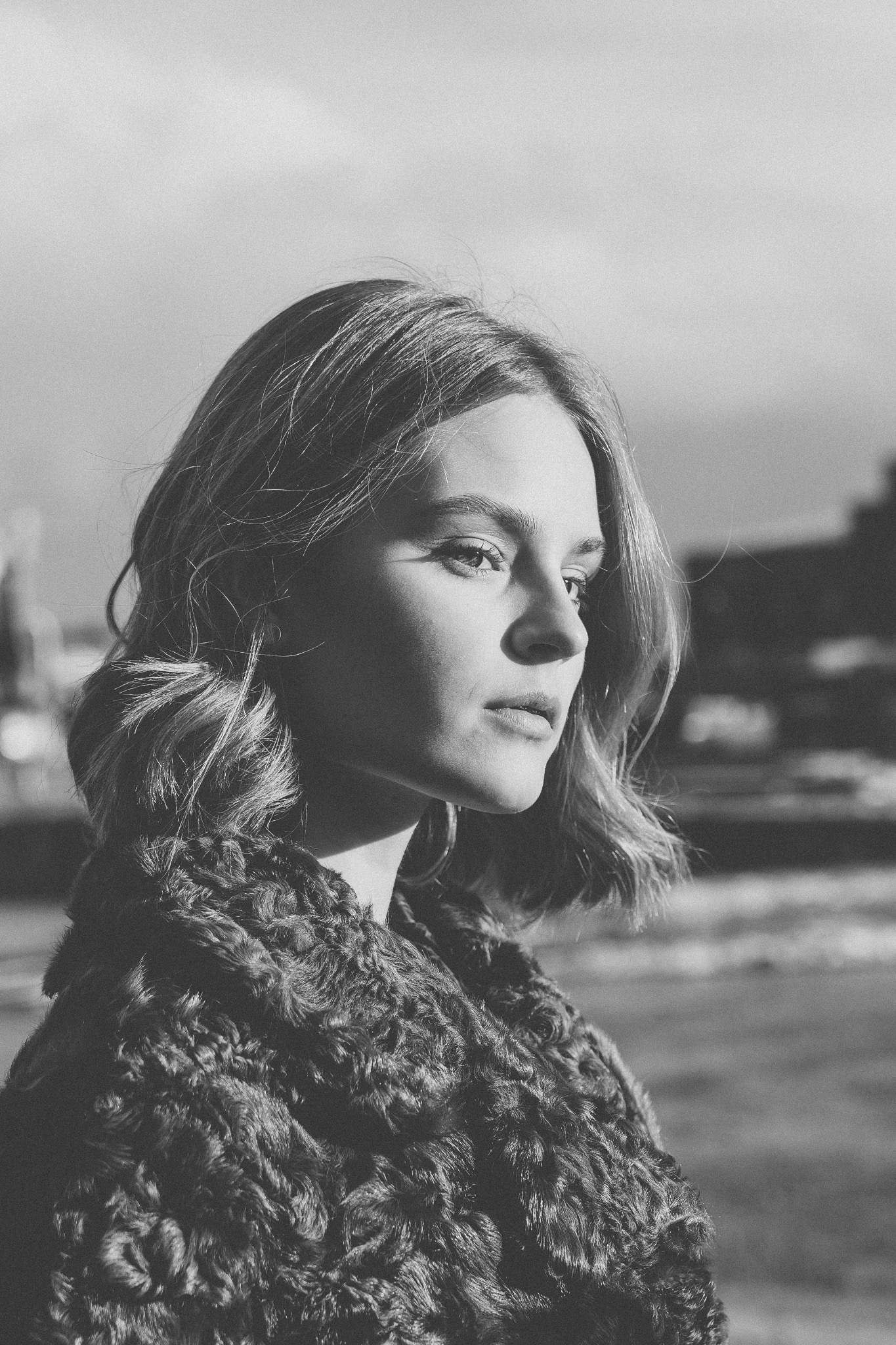 Portret kobiety w futrzanym płaszczu, spoglądającej w lewo, w czerni i bieli, z rozproszonym światłem padającym na twarz.