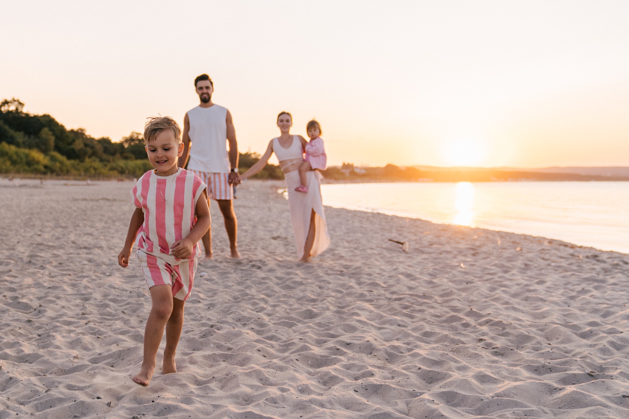 Rodzina na plaży w Gdańsku podczas zachodu słońca: chłopiec biegnie przodem, rodzice z małą dziewczynką w tle.